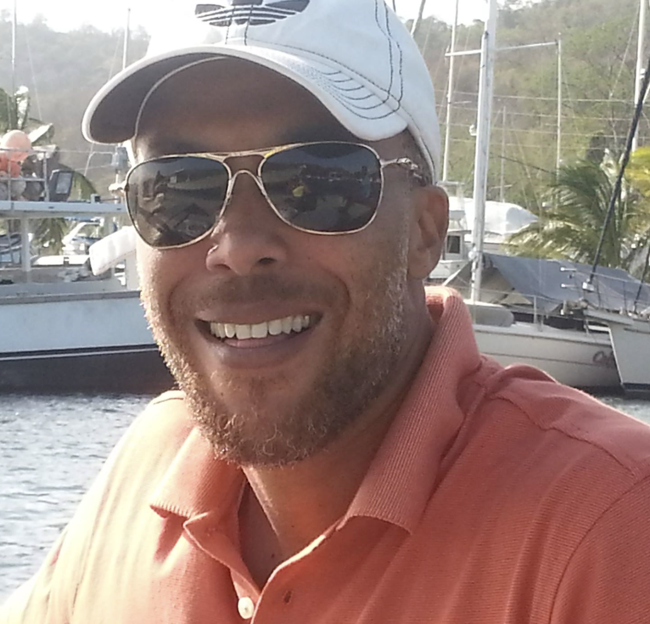 Young guy smiling wearing orange polo shirt sitting at a marina